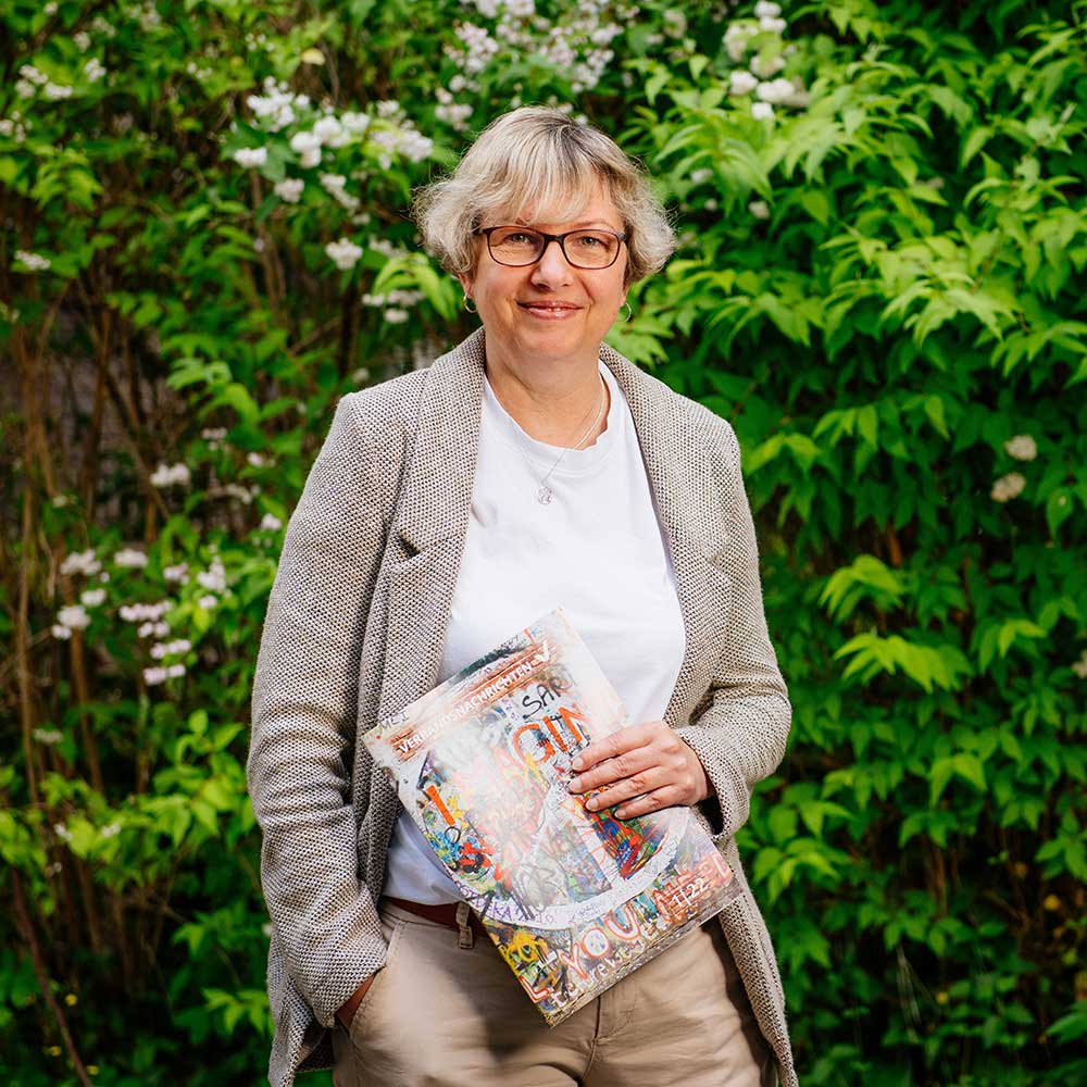 Frau mit Brosch&uuml;re in der Hand steht im Gr&uuml;nen.
