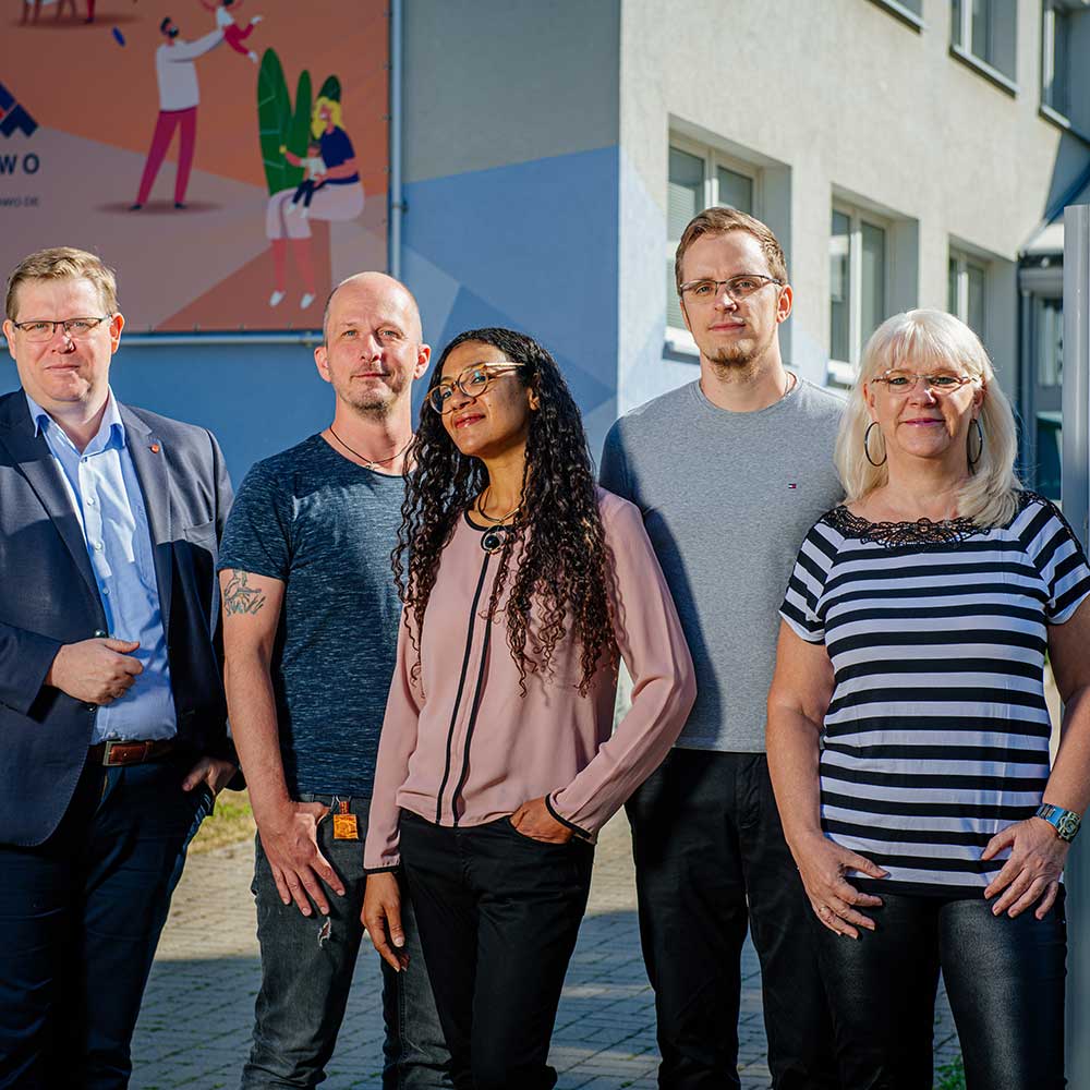 Drei Männer und zwei Frauen stehen vor einem blau bemalten Wohnblock.