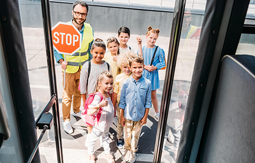 Kinder stehen mit Sch&uuml;lerlotsen vor dem Eingang eines Busses.