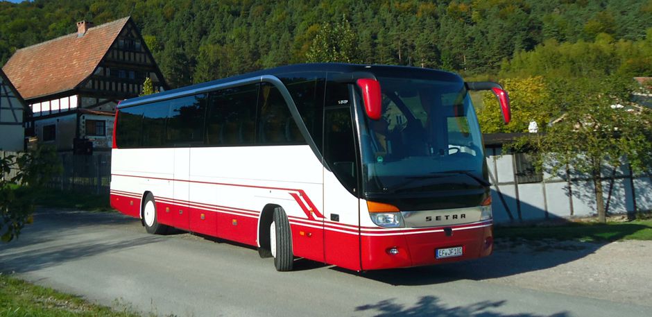 Reisebus mit weißer und roter Lackierung im Grünen.