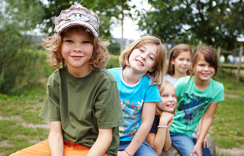 F&uuml;nf l&auml;chelnde Kinder sitzen hintereinander im Gr&uuml;nen und schauen in die Kamera.