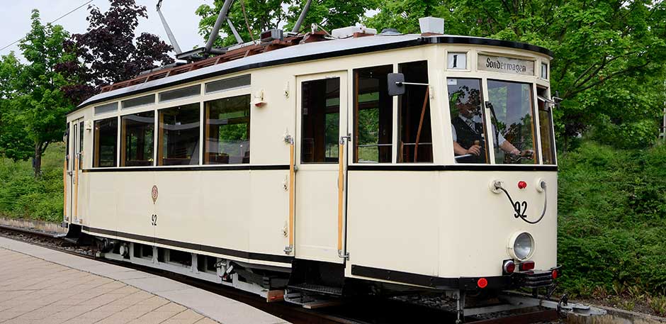 Historische Straßenbahn Nummer 92 in beiger Lackierung in der Wendeschleife. Im Hintergrund grüne Bäume.