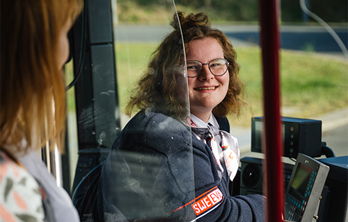 Junge Busfahrerin sitzt am Steuer und l&auml;chelt Fahrgast an.