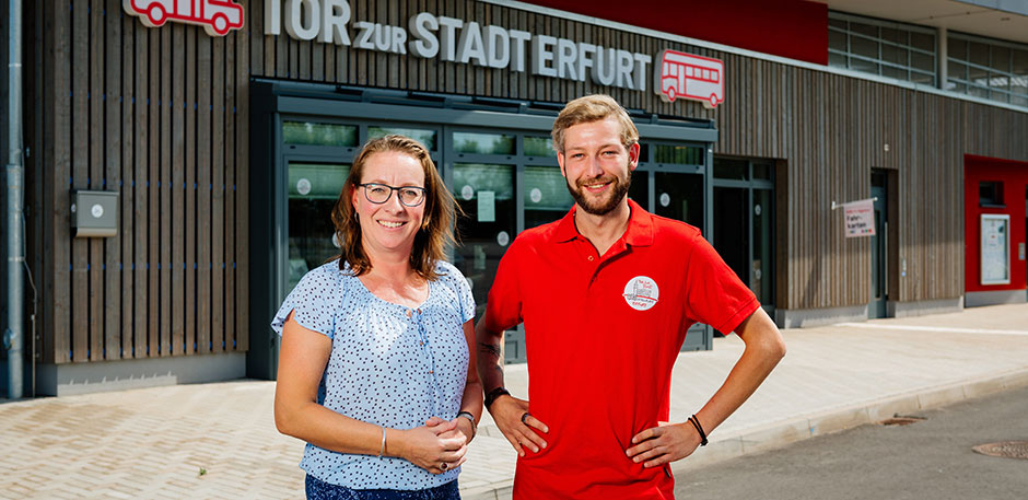 Frau und Mann stehen vor einem Empfangsgebäude auf dem "Tor zur Stadt Erfurt" steht.
