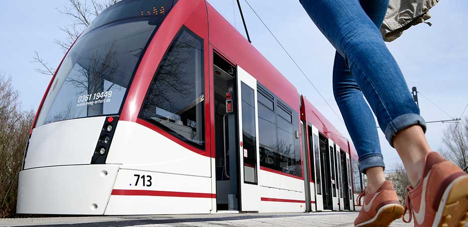 Straßenbahn mit geöffneter Tür. Rechts im Vordergrund ein rennender Fahrgast.