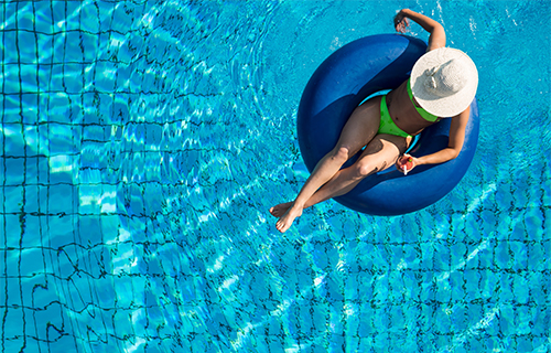 Frau mit Bikini und Sonnenhut auf Schwimmreifen im Pool.