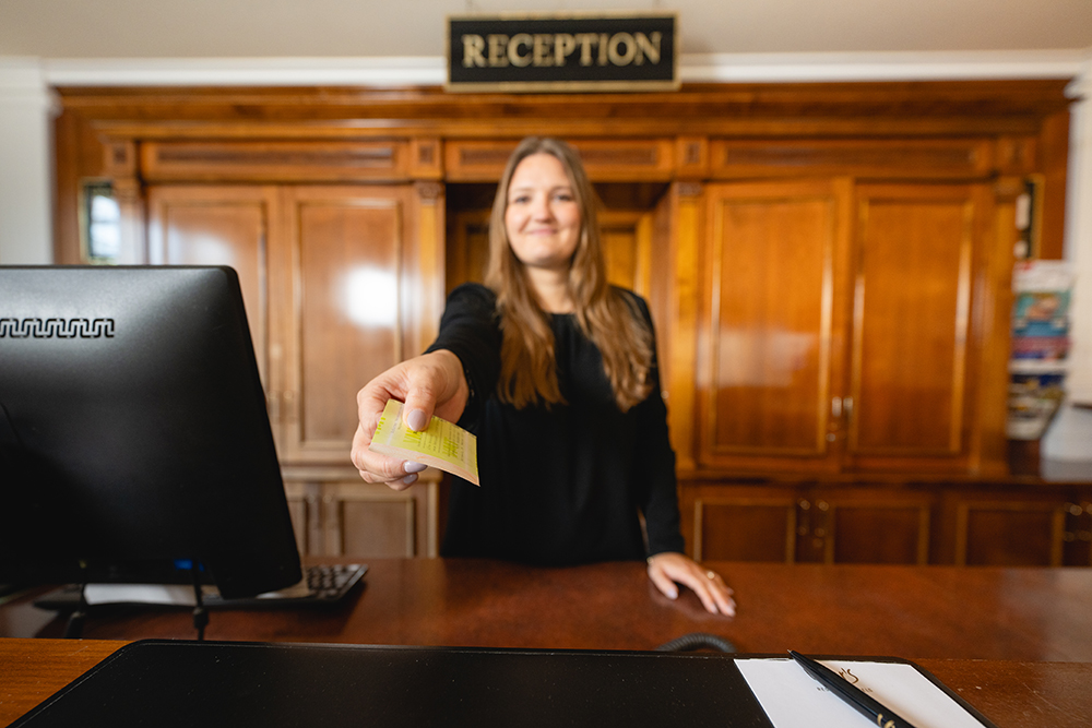 Junge Frau an der Rezeption h&auml;lt einen Fahrschein in der Hand.