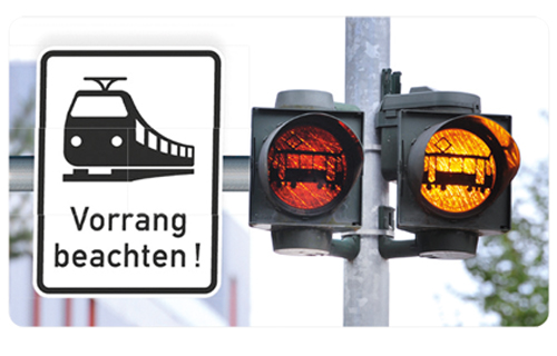 Links Schild mit Piktogramm Tram und Hinweis "Vorrang beachten". Rechts gelb leuchtender Doppelblinker.