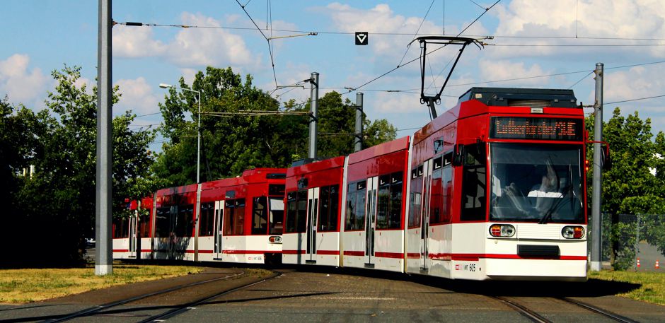 Moderne Straßenbahn in roter und weißer Lackierung in Wendeschleife. Im Hintergrund grüne Bäume.