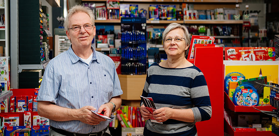 Mann und Frau stehen in einem Zeitschriftenladen. Beide halten Flyer in der Hand .