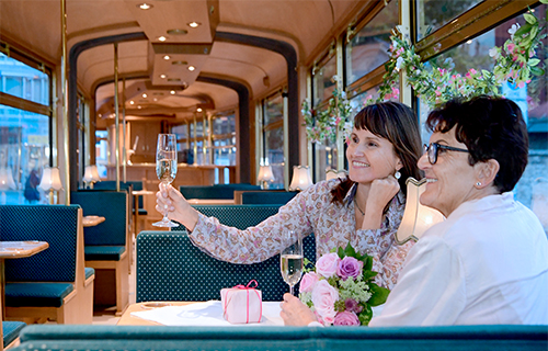 Mutter und Tochter im Katerexpress mit Blumen und Sekt in der Hand. 