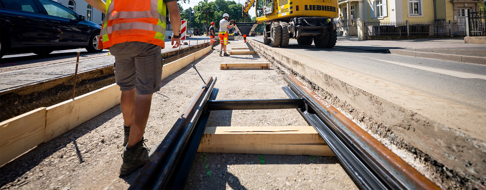 Stra&szlig;enbauarbeiten mit verlegten Schienen, Bauarbeitern in Warnwesten und Bagger auf einer innerst&auml;dtischen Baustelle