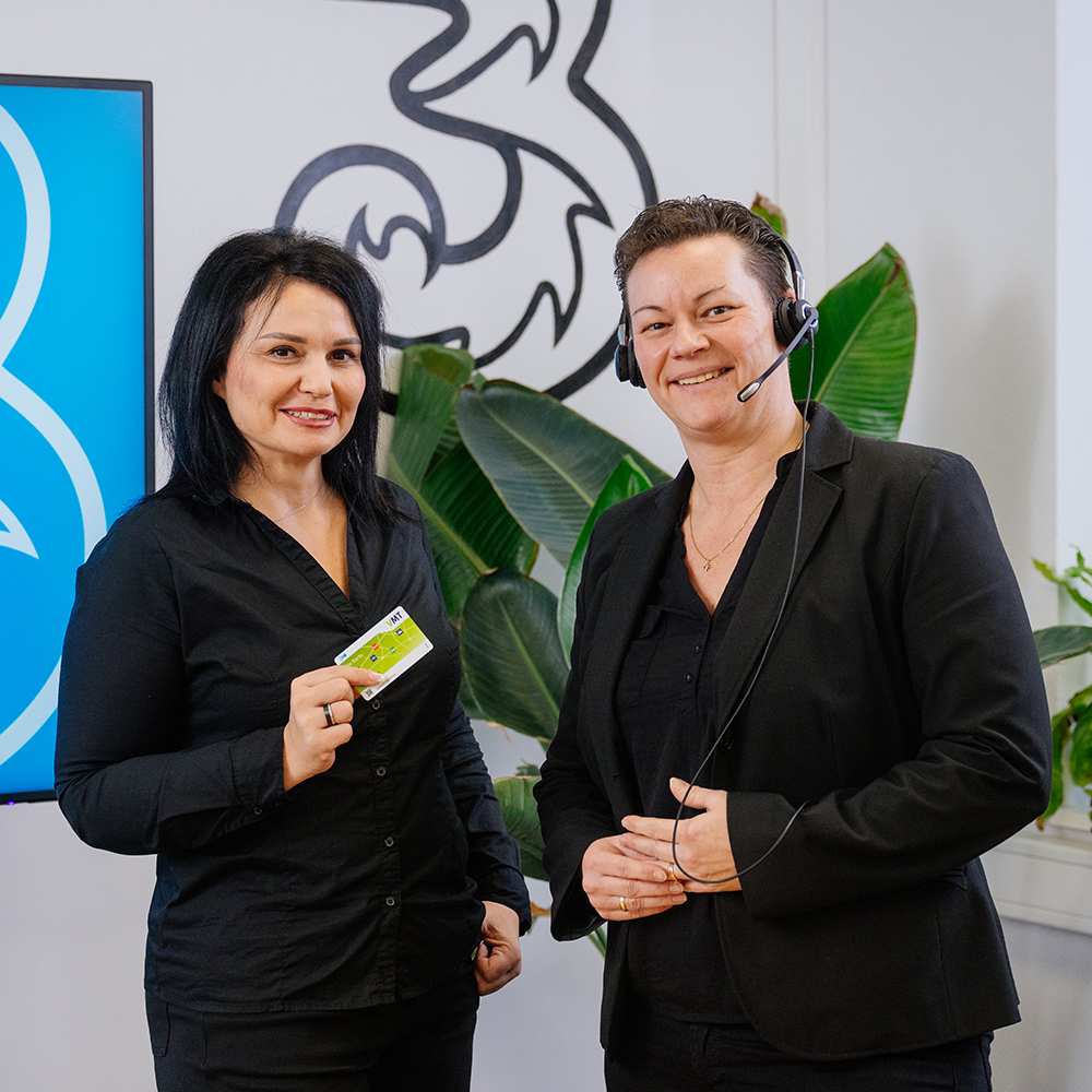 Zwei Frauen stehen vor einer Zimmerpflanze. Eine Frau h&auml;lt eine gr&uuml;ne Chipkarte in der Hand.