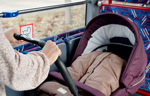 Kinderwagen auf gekennzeichnetem Stellplatz im Bus. Mutter hält den Kinderwagen fest.
