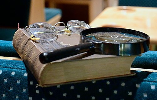 Altes Buch, Brille und Lupe liegen auf einem Sitz in historischer Stra&szlig;enbahn.